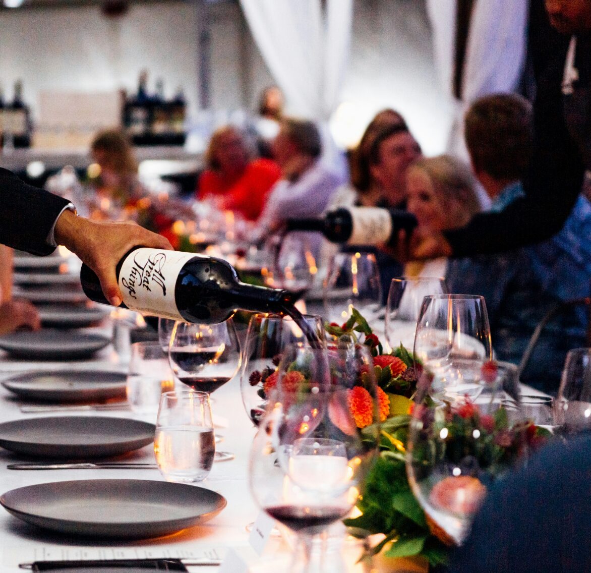Guests seated at a long dinner table as wine is poured